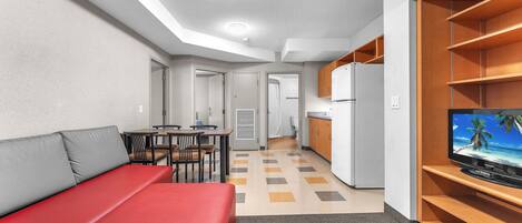 Un espacio habitable compacto con kitchenette, comedor y sala de estar con sofá y sillas rojas.