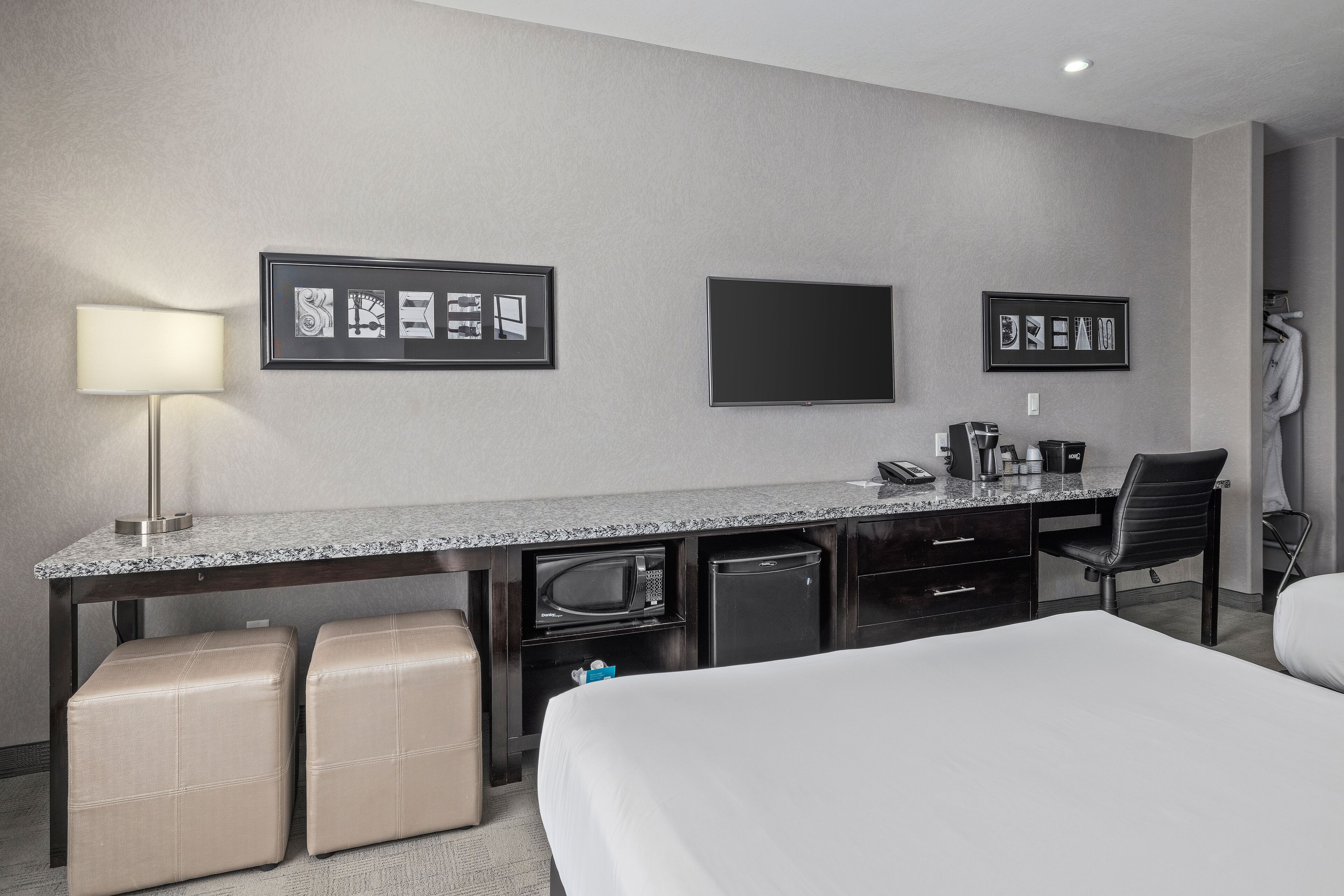 A hotel room with a bed, a desk with a lamp, a television, and a minibar.