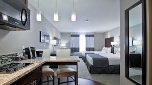 Habitación de hotel con cocina, dos camas, un espejo grande y vistas al exterior.