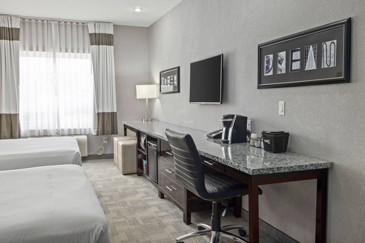 A hotel room with two beds, a desk with a chair, a TV, and a framed picture on the wall.