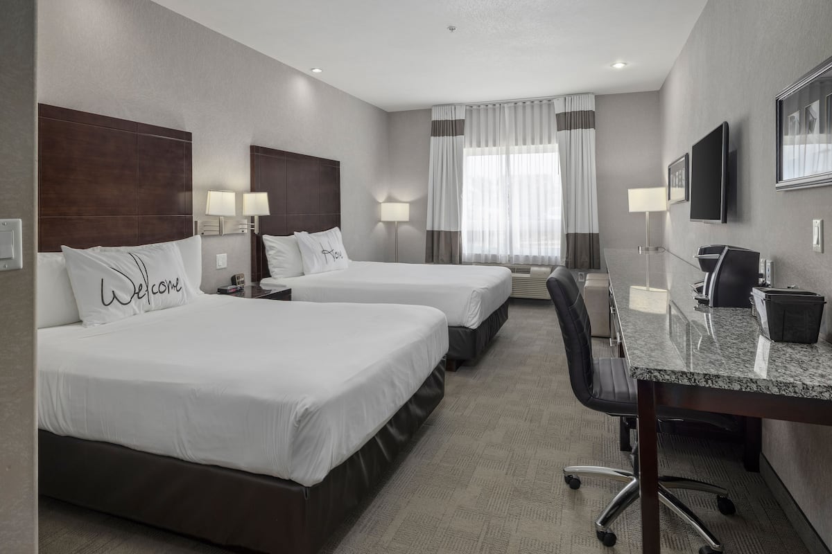 A hotel room with two beds, a desk, a chair, and a TV.