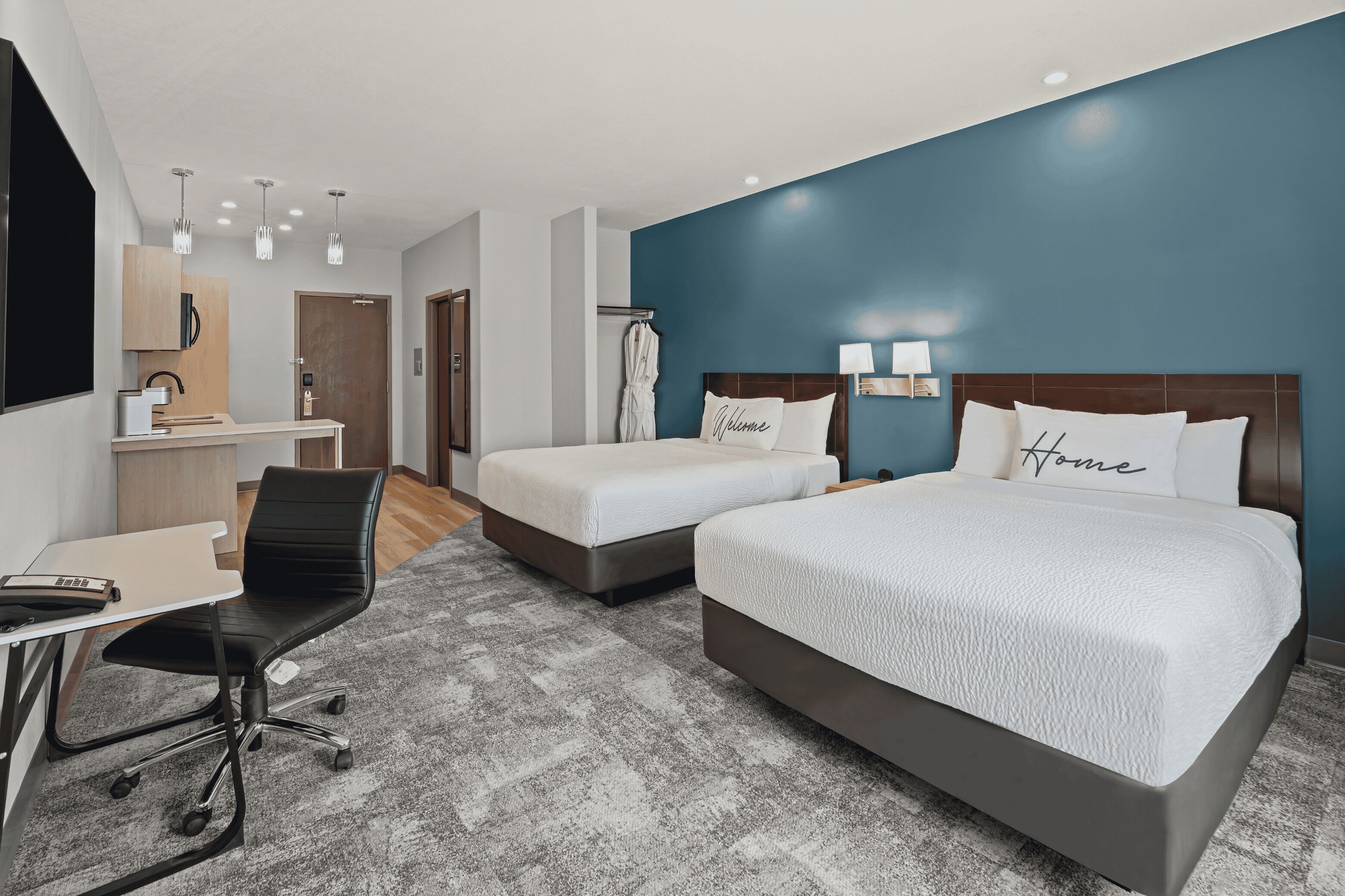 Habitación de hotel con dos camas, un escritorio, una silla y un televisor.
