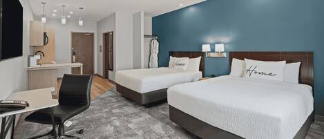 A hotel room with two beds, a desk, a chair, and a TV.
