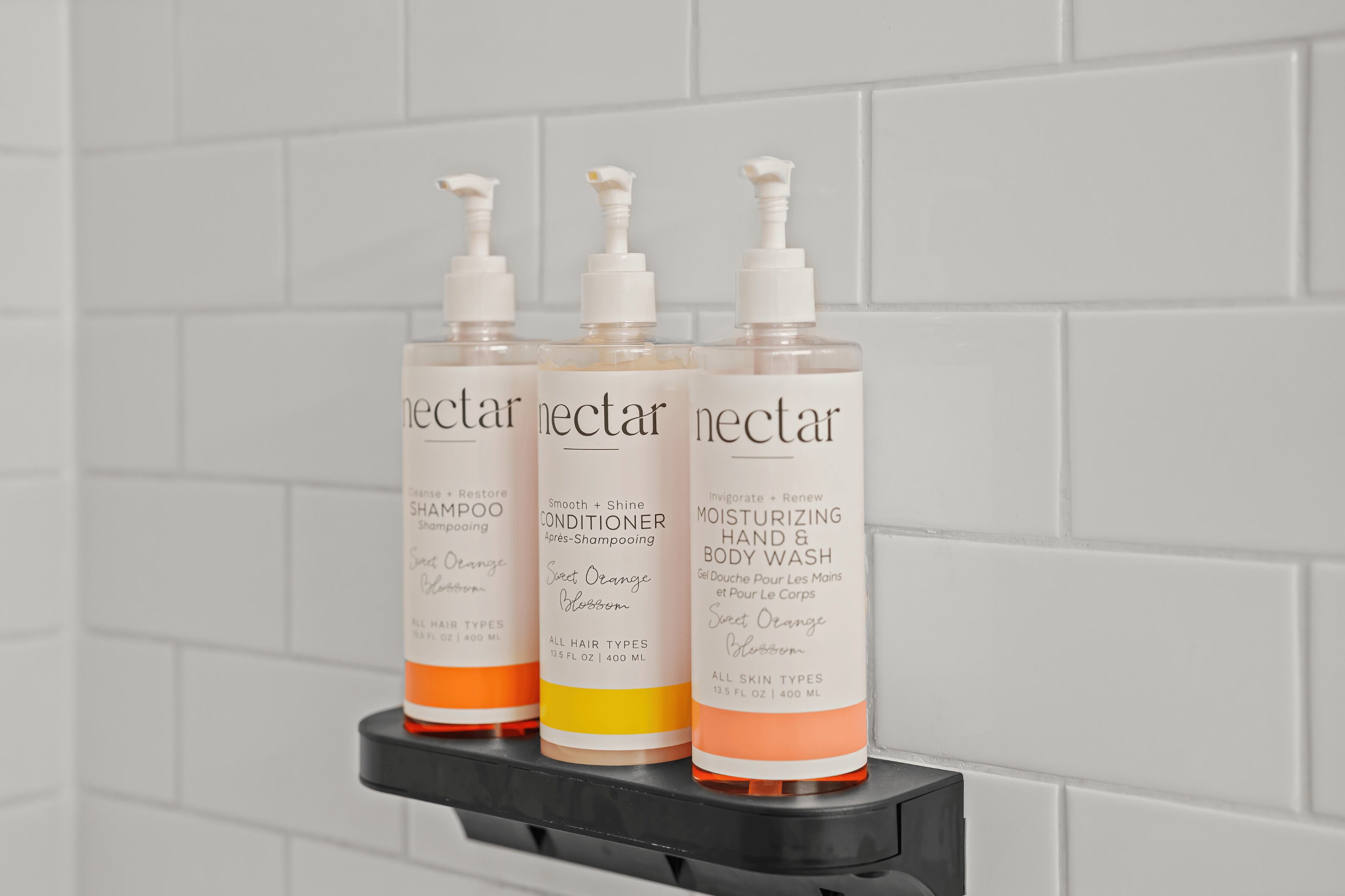 Tres botellas de productos Neclair sobre un estante negro frente a una pared de azulejos blancos.