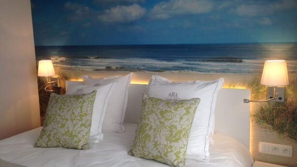 A bedroom with a bed, pillows, and wall-mounted lamps. - Ara Dune Hotel (De Panne)