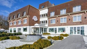 A hotel with a brick facade, a central courtyard with a circular water feature, and a sign reading "ARA COSY HOME". - Ara Dune Hotel (De Panne)