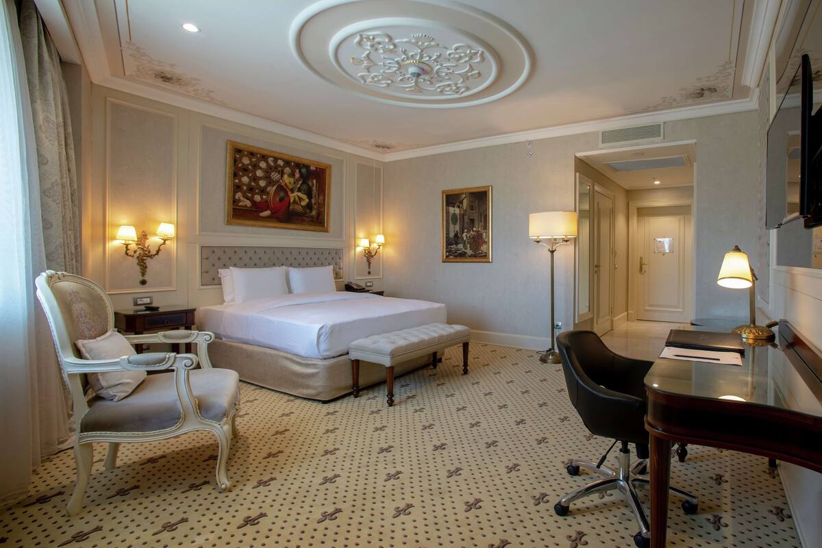 A hotel room with a bed, a desk, a chair, and two wall-mounted lamps.