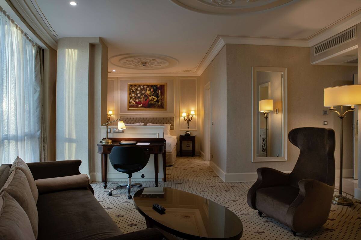 A hotel room with a sofa, armchair, coffee table, desk, and a bed.