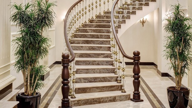 Una imponente escalera con acabado de mármol, flanqueada por plantas en macetas y un gran candelabro.