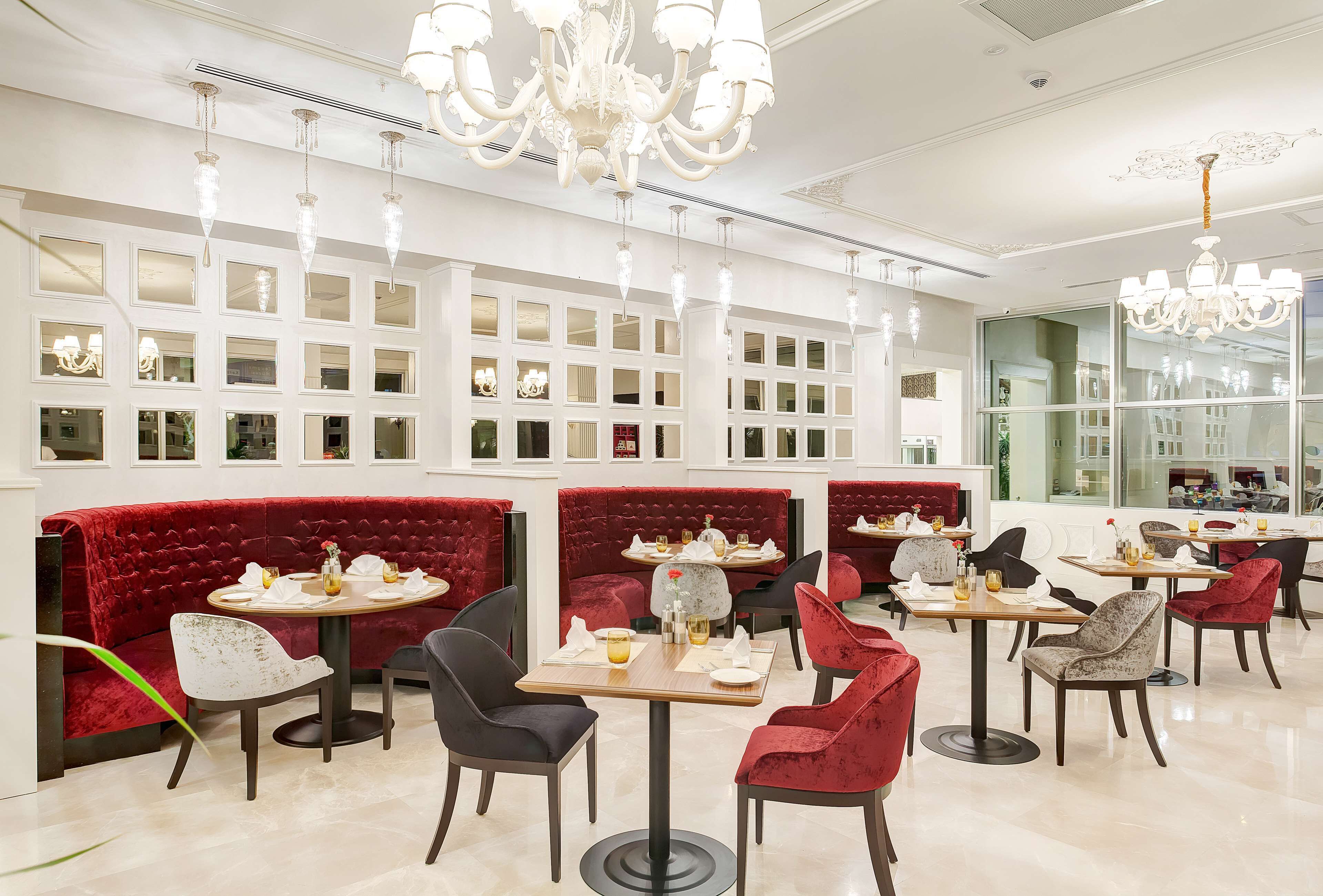 Un restaurante con cabinas de terciopelo rojo, candelabros blancos y un diseño de interiores moderno.