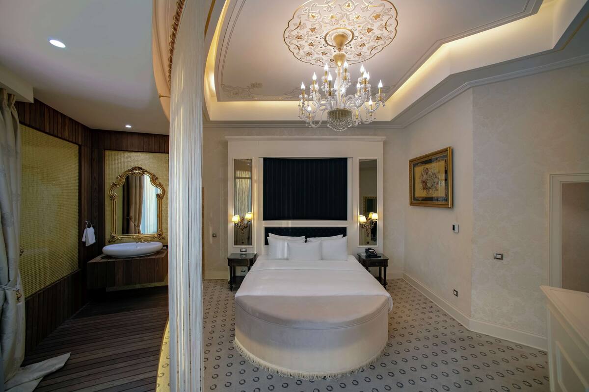 A hotel room with a large bed, a chandelier, a mirror, and a painting on the wall.