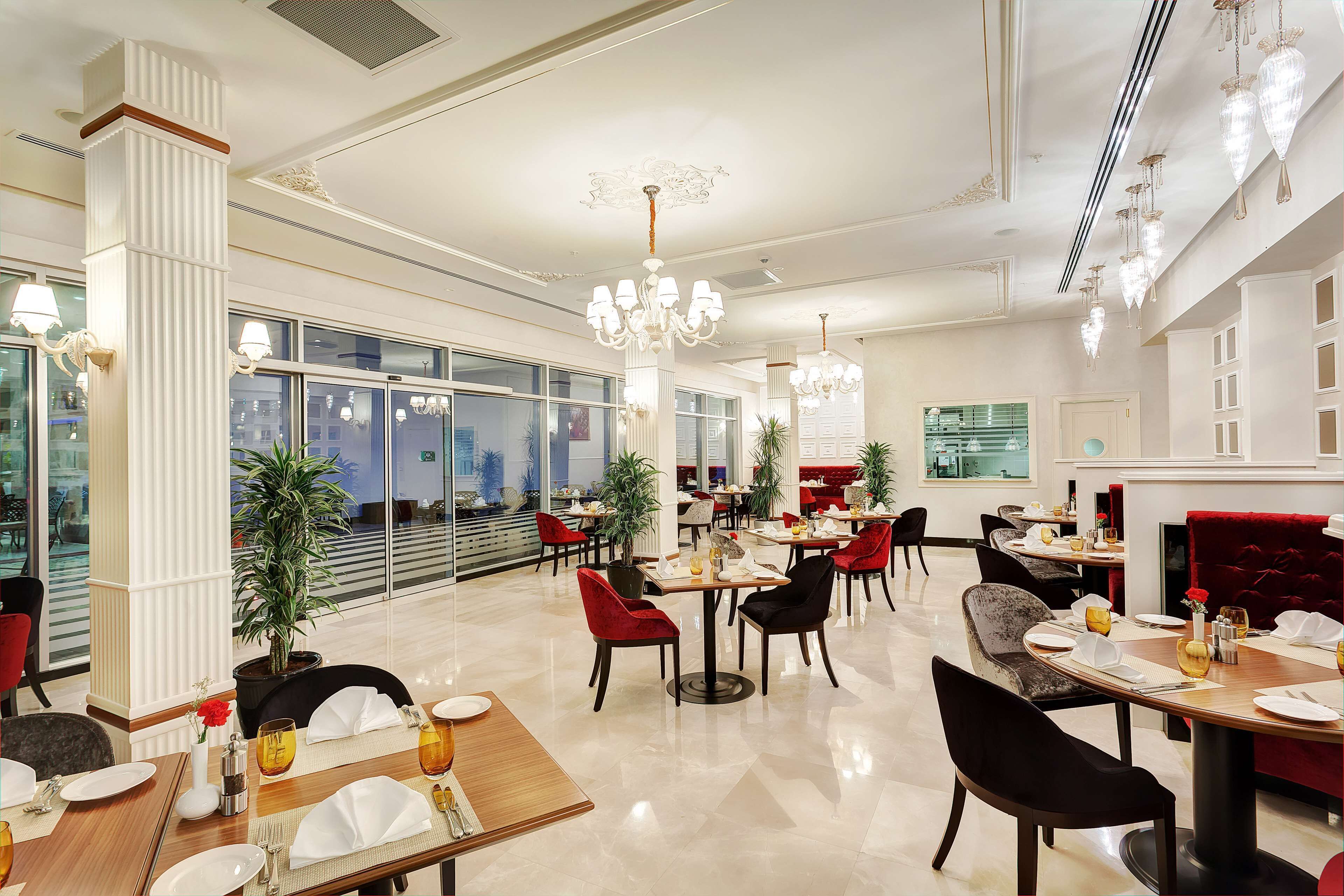 A modern restaurant with high ceilings, chandeliers, and a variety of seating arrangements.