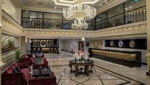 Un amplio vestíbulo con candelabro, asientos c ómodos, un mostrador de recepción y una escalera.