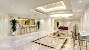 Un vestíbulo amplio con suelo de mármol, una lámpara central y una zona de buffet con un sofá rojo al fondo.