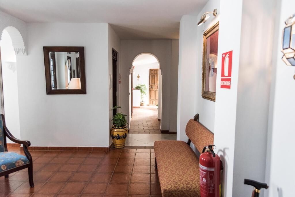 A hallway with a bench, a fire extinguisher, a mirror, and a potted plant.