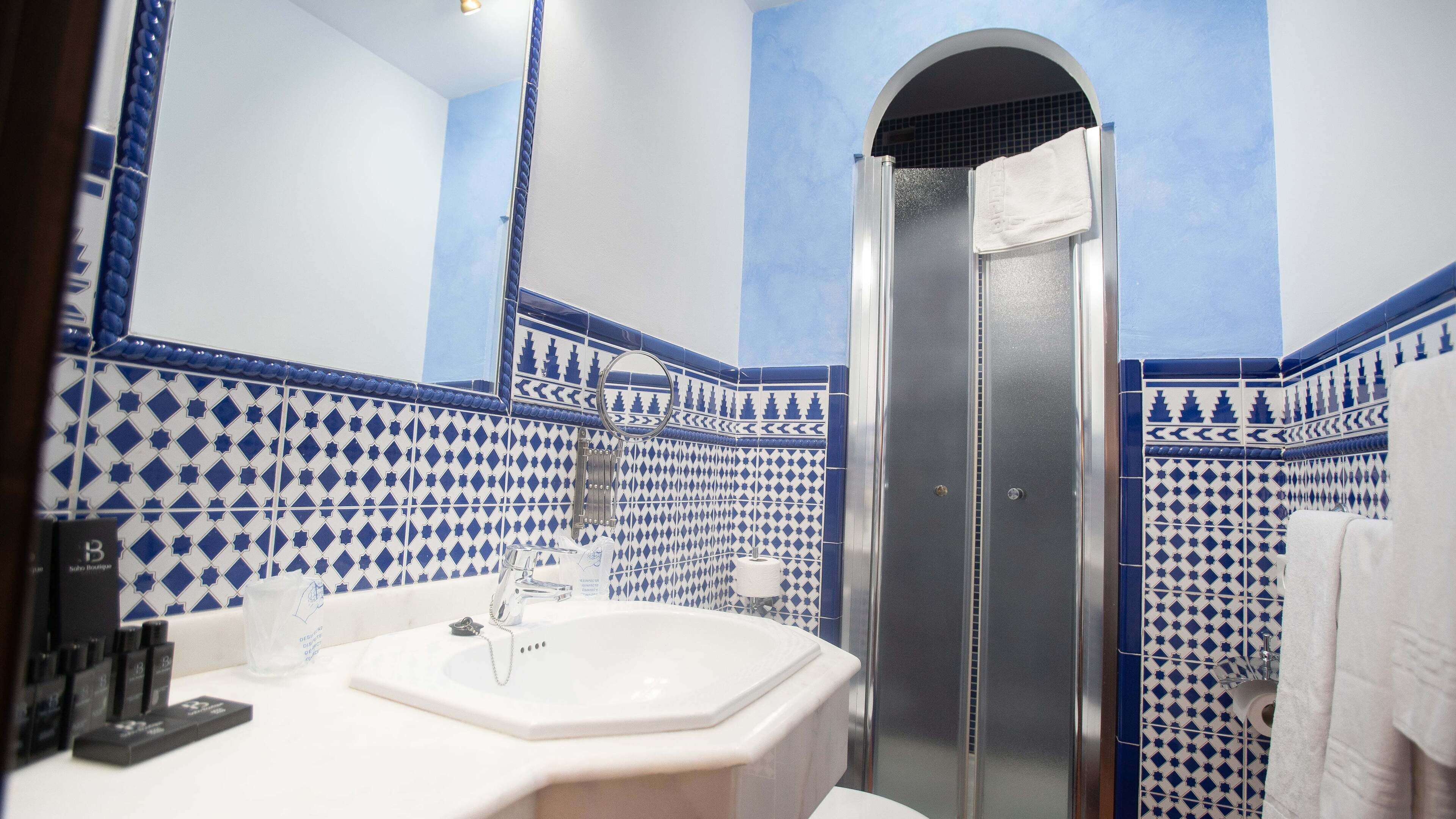 Un baño con un lavabo blanco, un espejo y una ducha. Las paredes están cubiertas de azulejos con diseños azules y blancos.