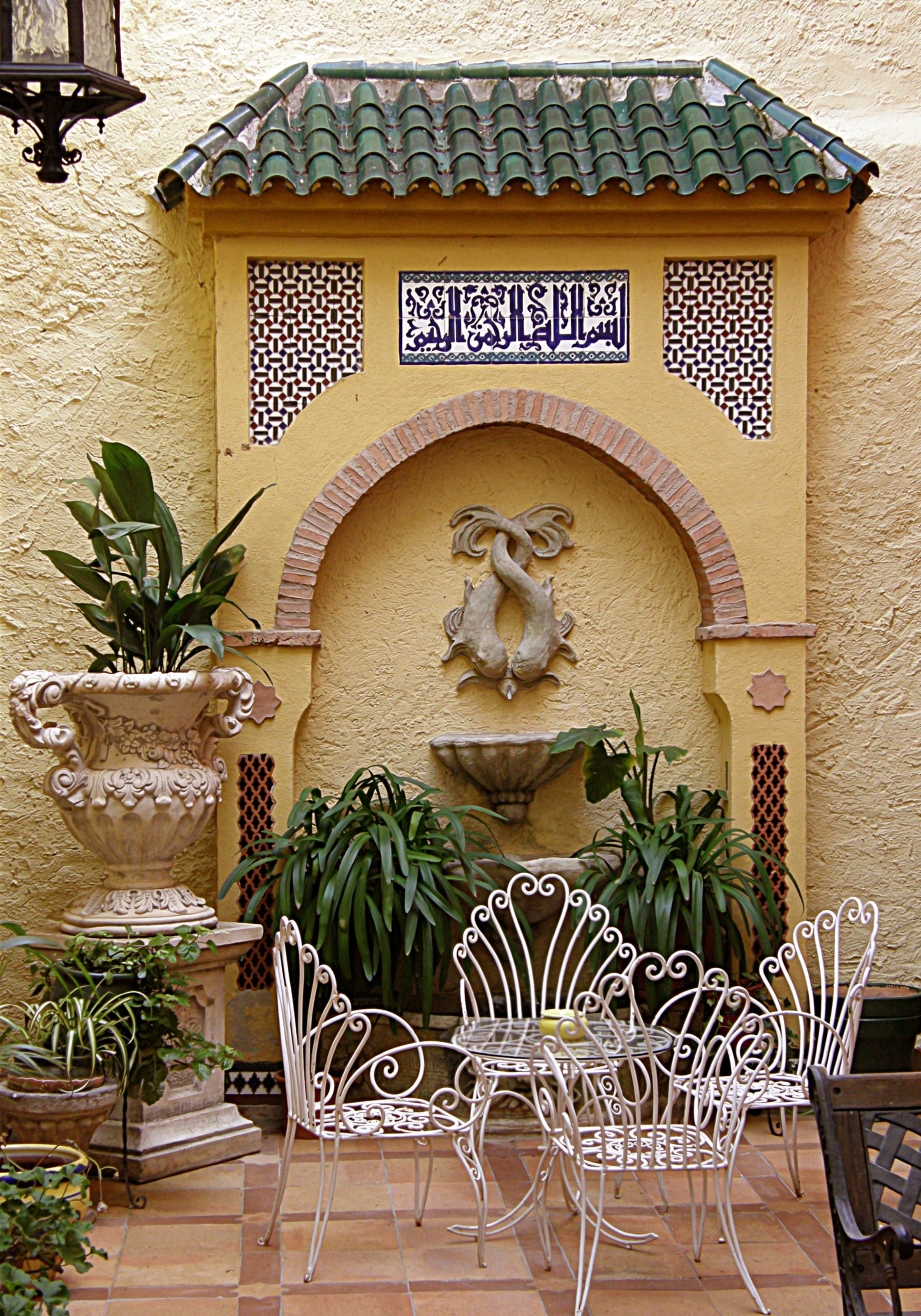 Un patio con suelo de baldosas, una fuente y una pared con azulejos decorativos y una figura de piedra tallada.
