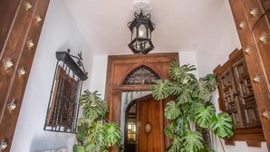 Une porte en bois surmontée d’une arche décorative, une lanterne suspendue et de grandes plantes vertes.