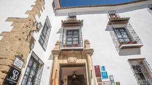 Un bâtiment à la façade blanche, doté de nombreuses fenêtres avec des barreaux en métal et de balcons. On y voit des drapeaux et des panneaux indiquant les services offerts par l’hôtel.