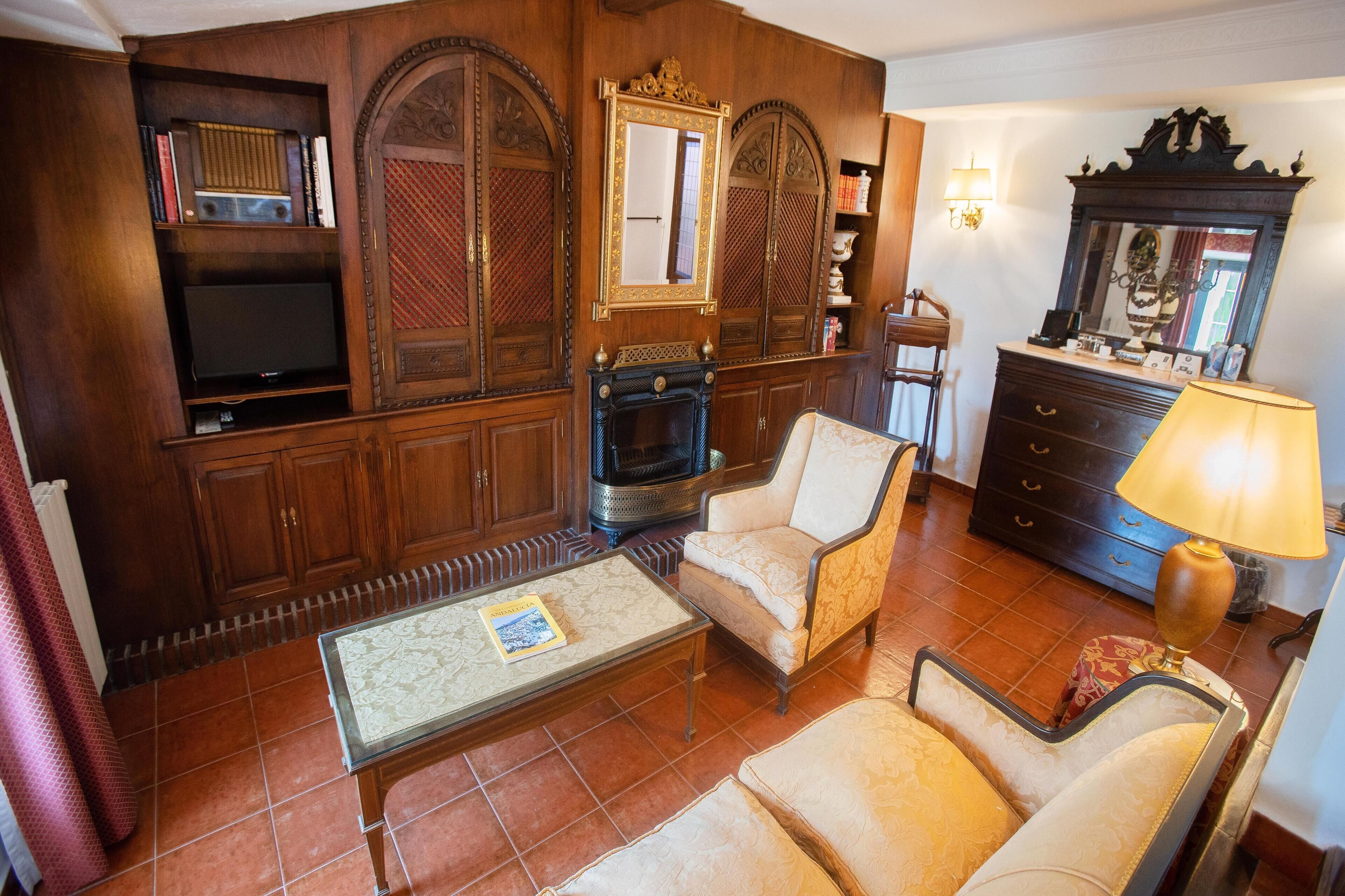A traditional living room with a fireplace, two armchairs, a coffee table, and a television.
