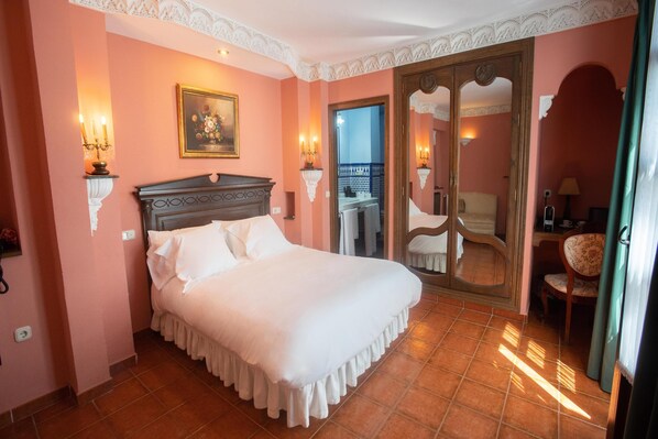 Un dormitorio con una cama grande, cabecera de madera, dos apliques, un cuadro enmarcado y una puerta al balcón.