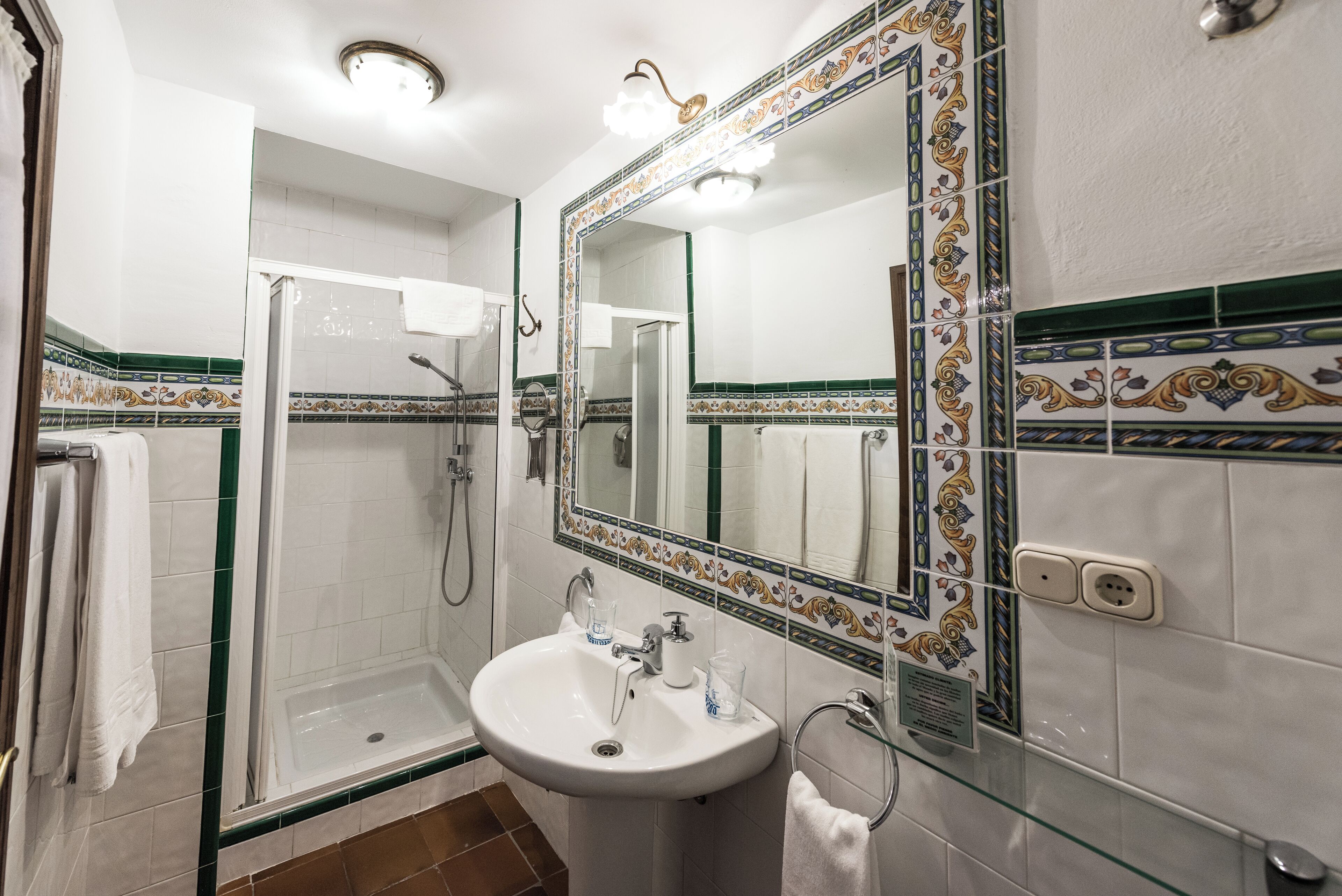 A bathroom with a glass-enclosed shower, a sink with a mirror, and decorative tiles.