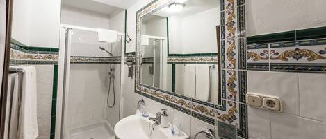 A bathroom with a glass-enclosed shower, a sink with a mirror, and decorative tiles.