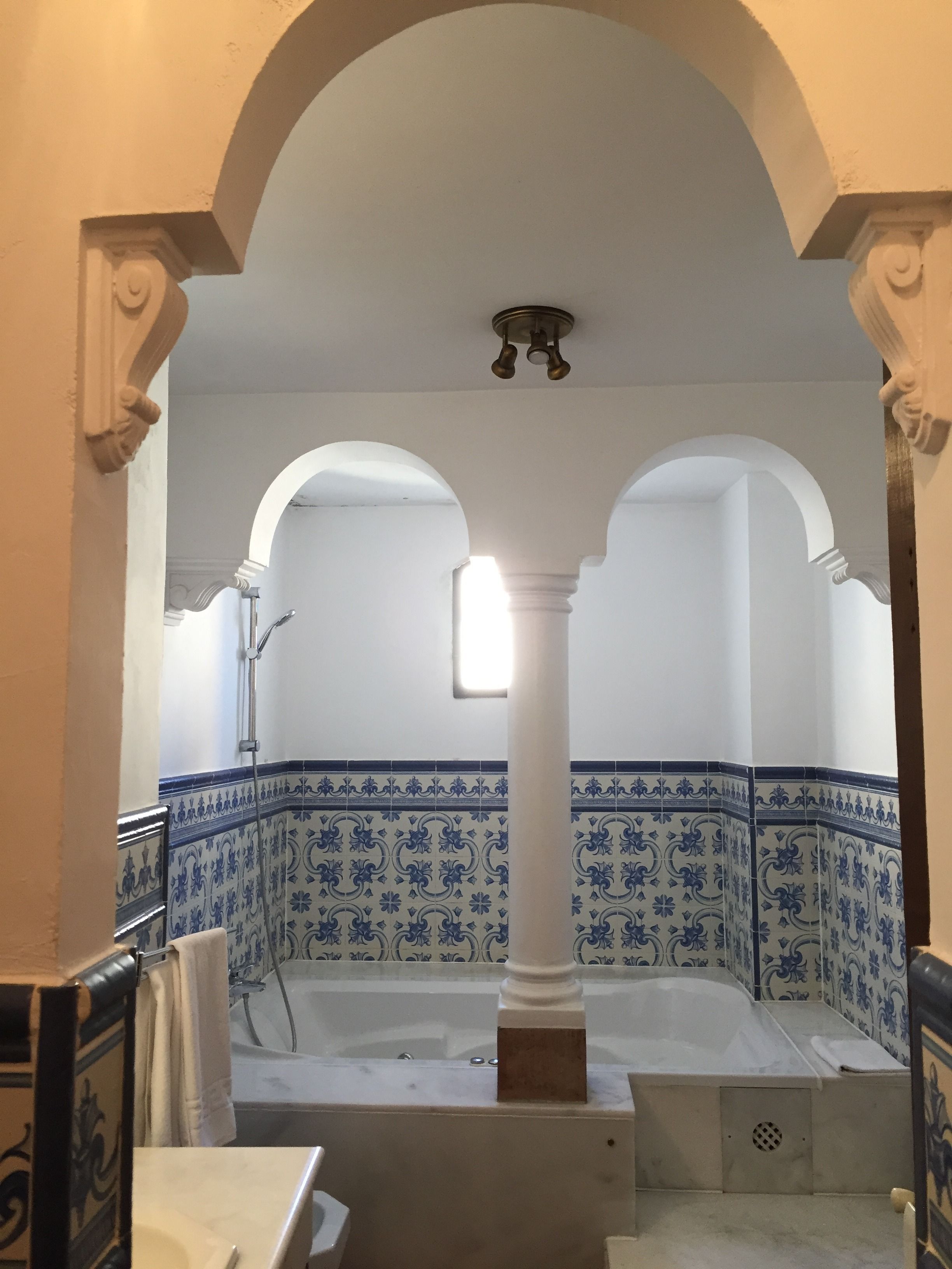 A bathroom with a bathtub, white columns, and blue patterned tiles.