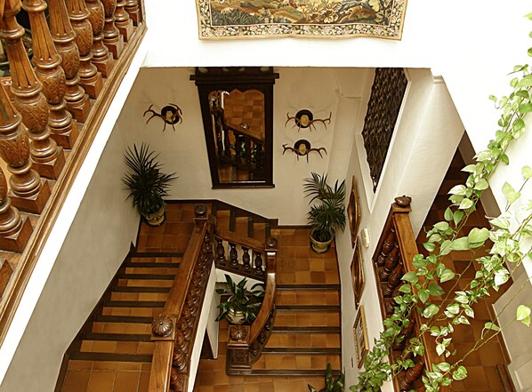 A grand staircase with ornate railings, multiple potted plants, and decorative wall art. - Soho Boutique Palacio San Gabriel (Ronda)