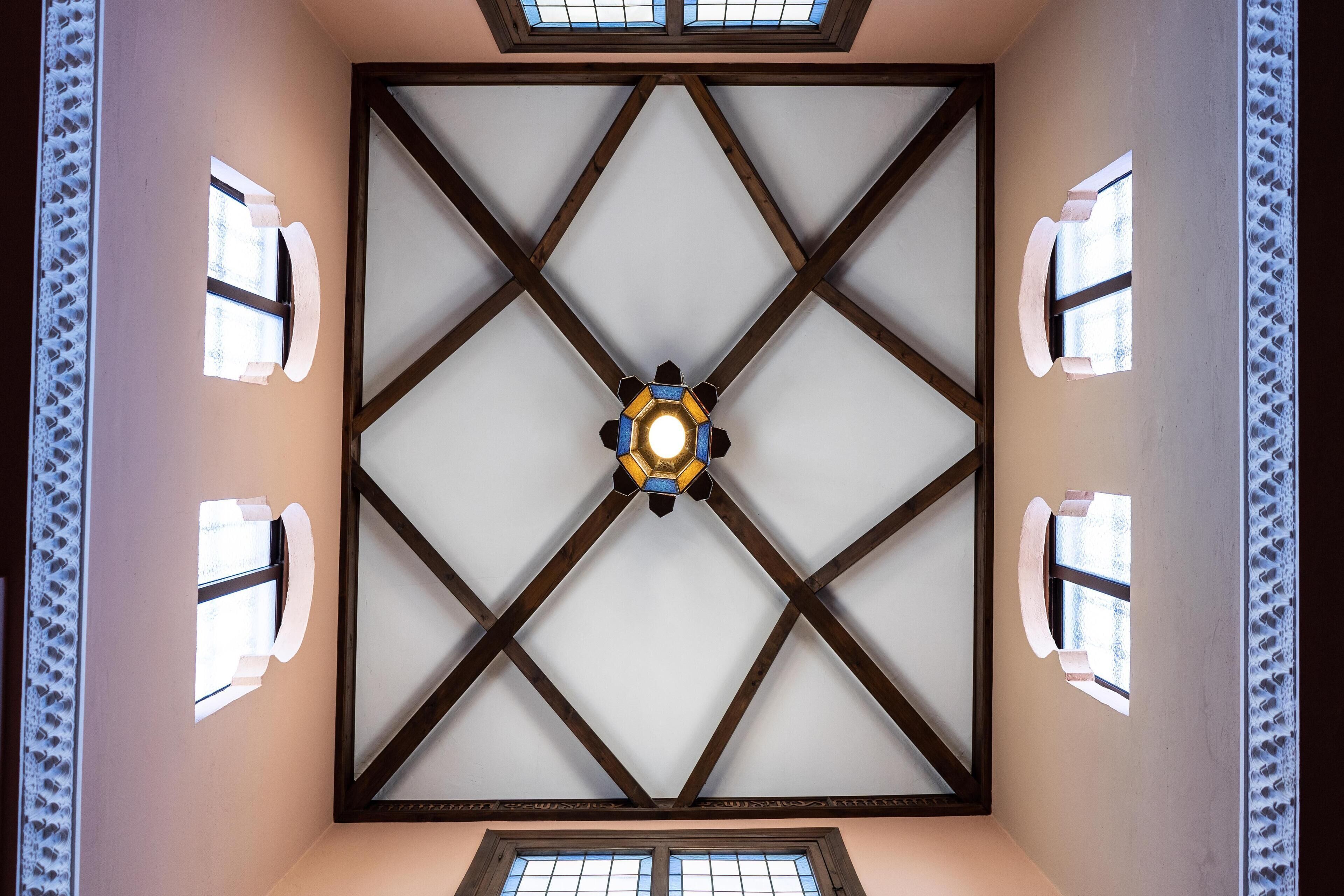 A room with a high ceiling featuring a geometric wooden framework and a central light fixture.