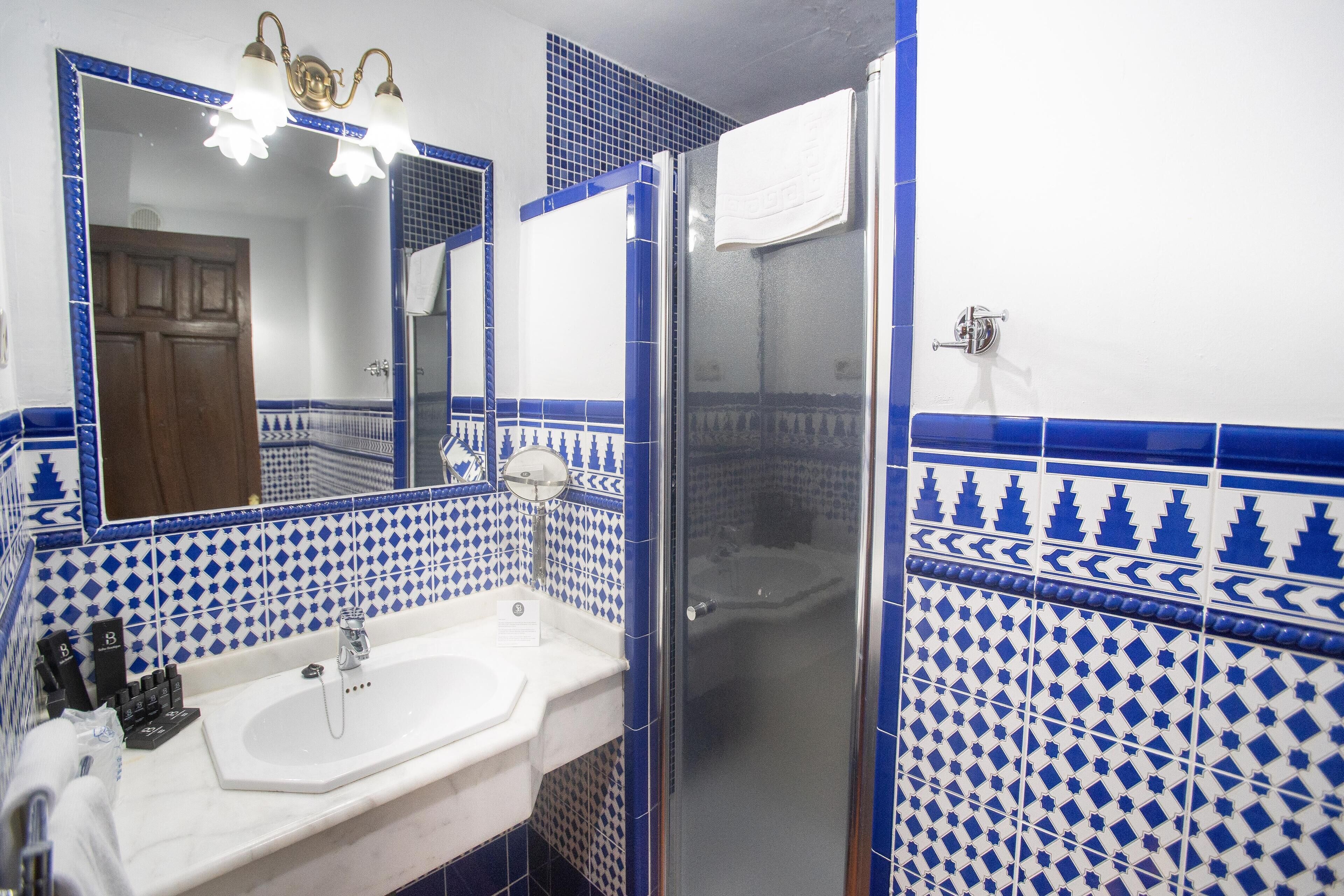Un baño con lavamanos blanco, espejo y azulejos azules con diseño.