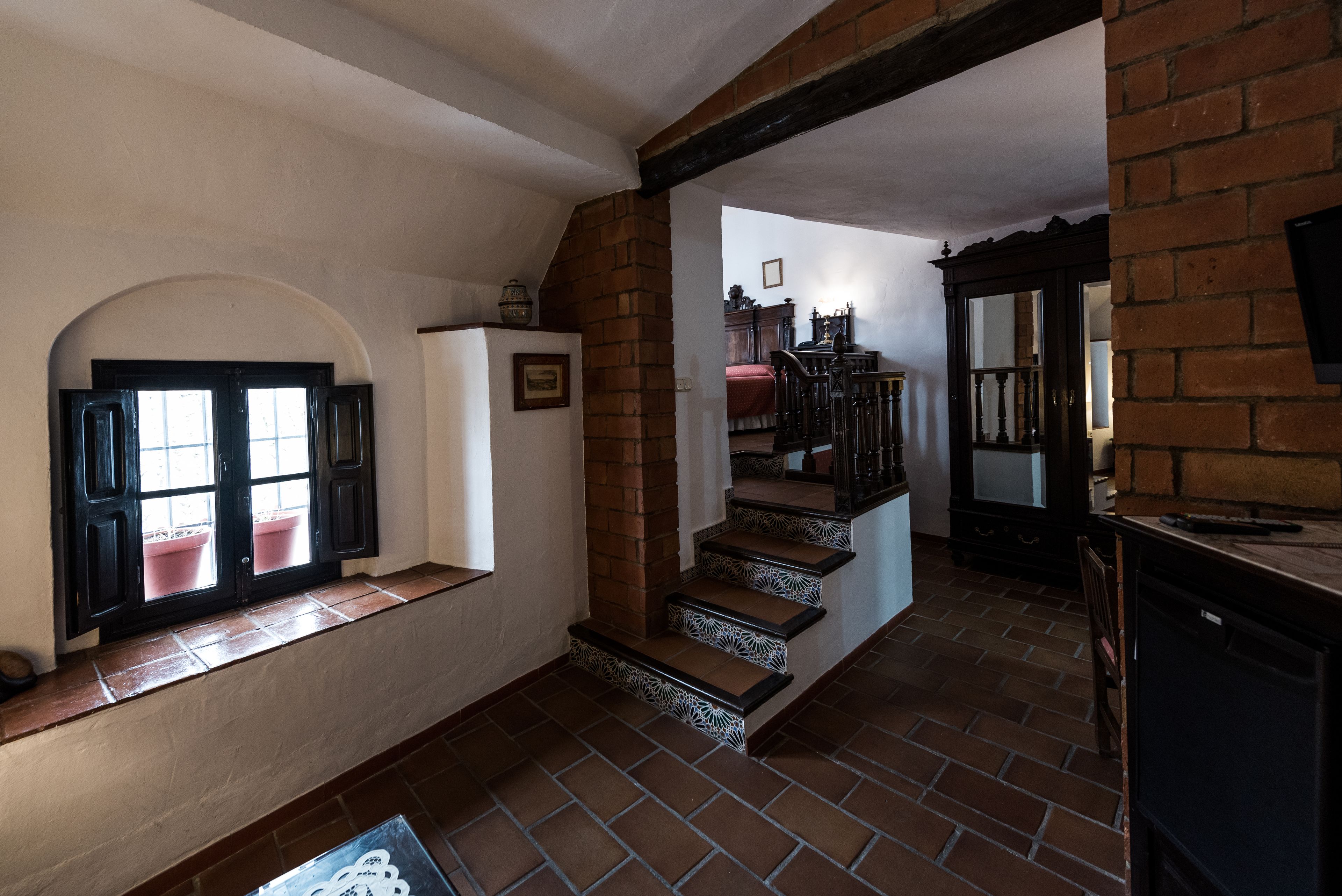A hallway with a brick staircase, a window with shutters, and a door leading to another room.