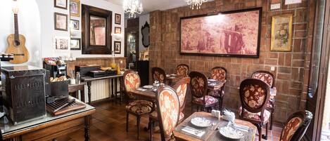 A dining area with a brick wall, wooden chairs, and a large painting.