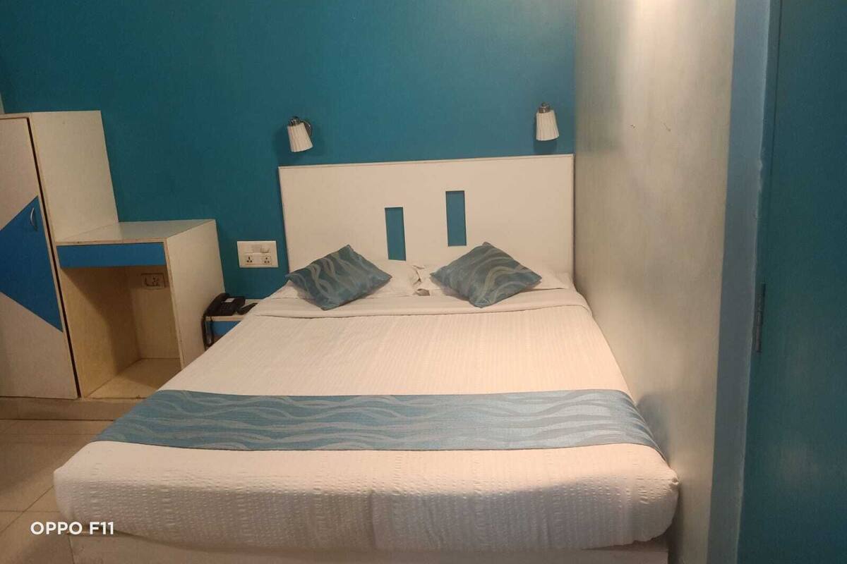 A neatly made bed with a blue and white bedspread, two pillows, and a bedside lamp.