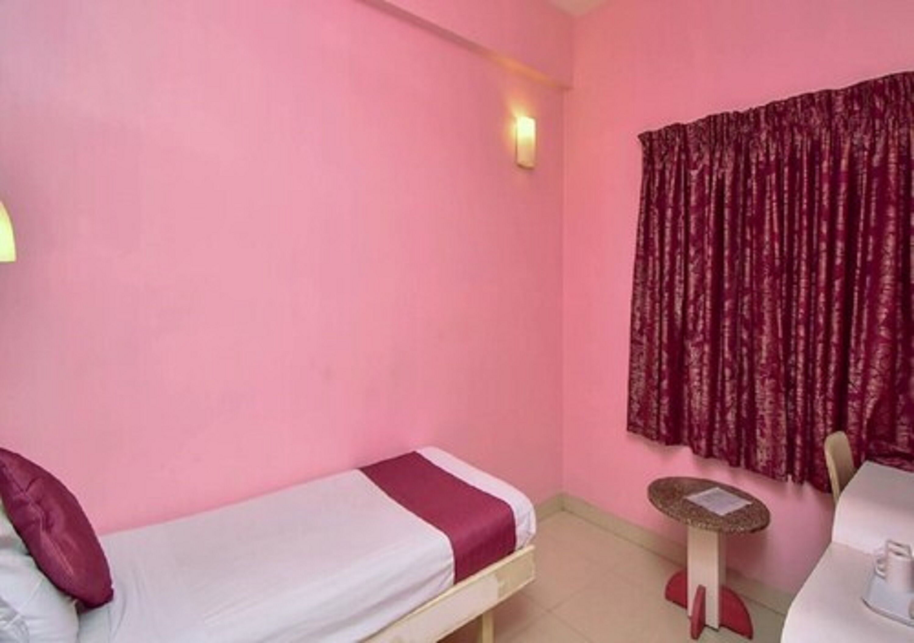A small room with a single bed, a small table, and a window with curtains.