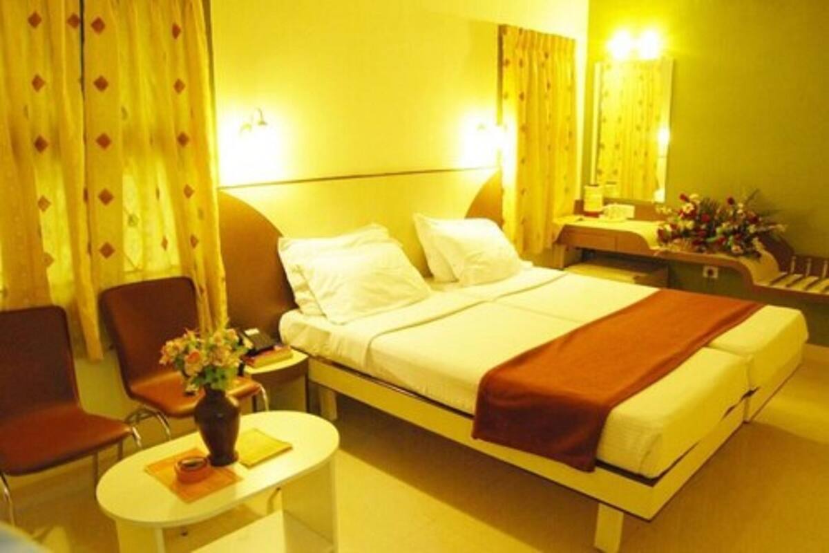 A hotel room with a bed, a chair, a small table with a vase of flowers, and a nightstand with a lamp.