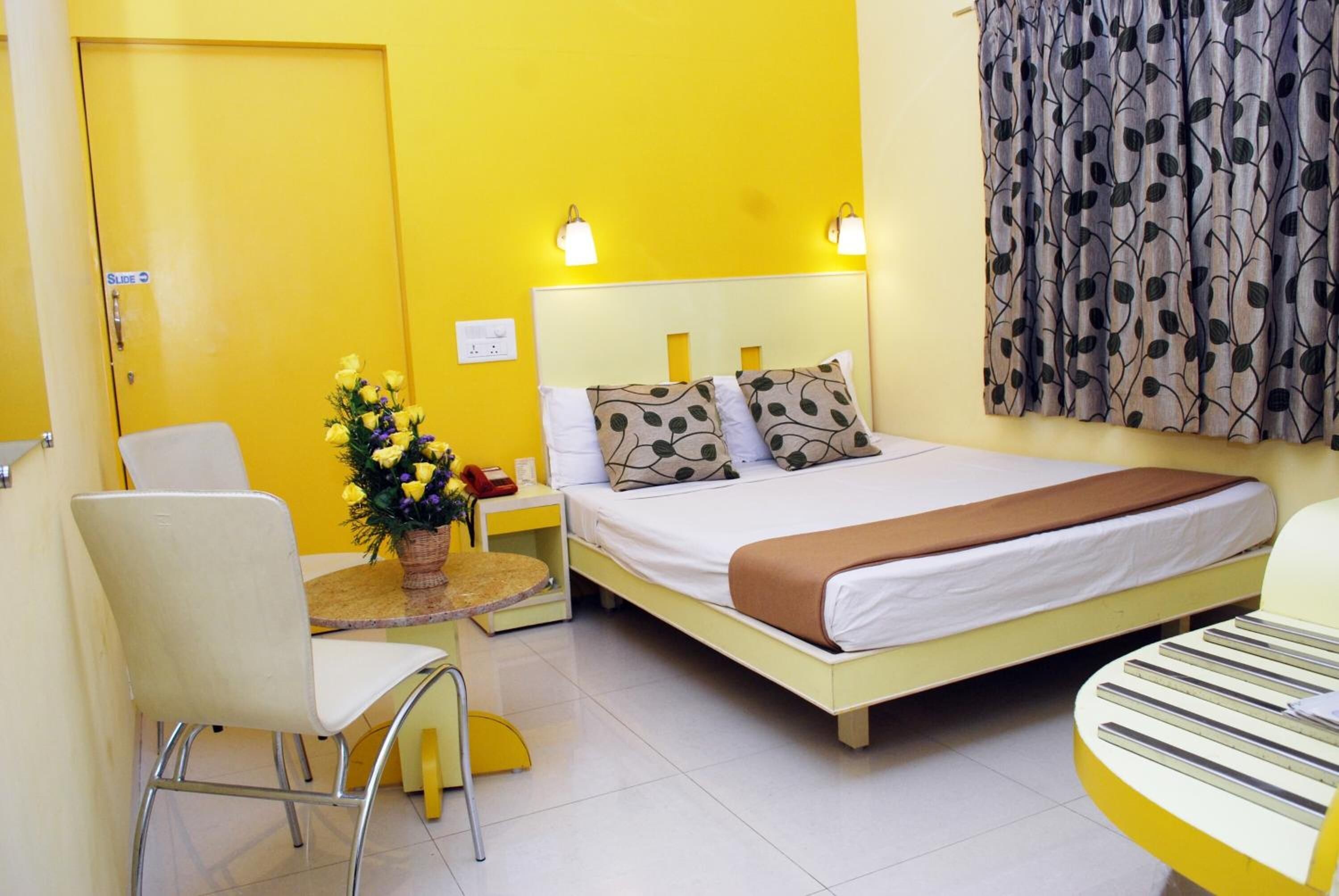 Quarto de hotel com cama, uma cadeira, uma mesa pequena e mesa de cabeceira com abajur.