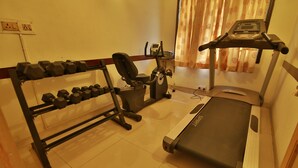 A home gym with a treadmill, dumbbells, and a stationary bike. - Hotel Pandian (Chennai)