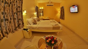 A hotel room with a bed, bedside tables, a TV, and a floral arrangement on the floor. - Hotel Pandian (Chennai)