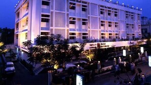 A multi-story hotel with a modern design, featuring a prominent rooftop structure and a well-lit entrance area. - Hotel Pandian (Chennai)