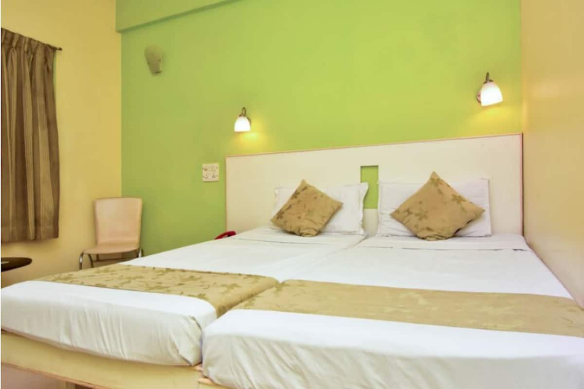 A double bed with two pillows, a bedside table, and a chair in a room with green walls and a white headboard.