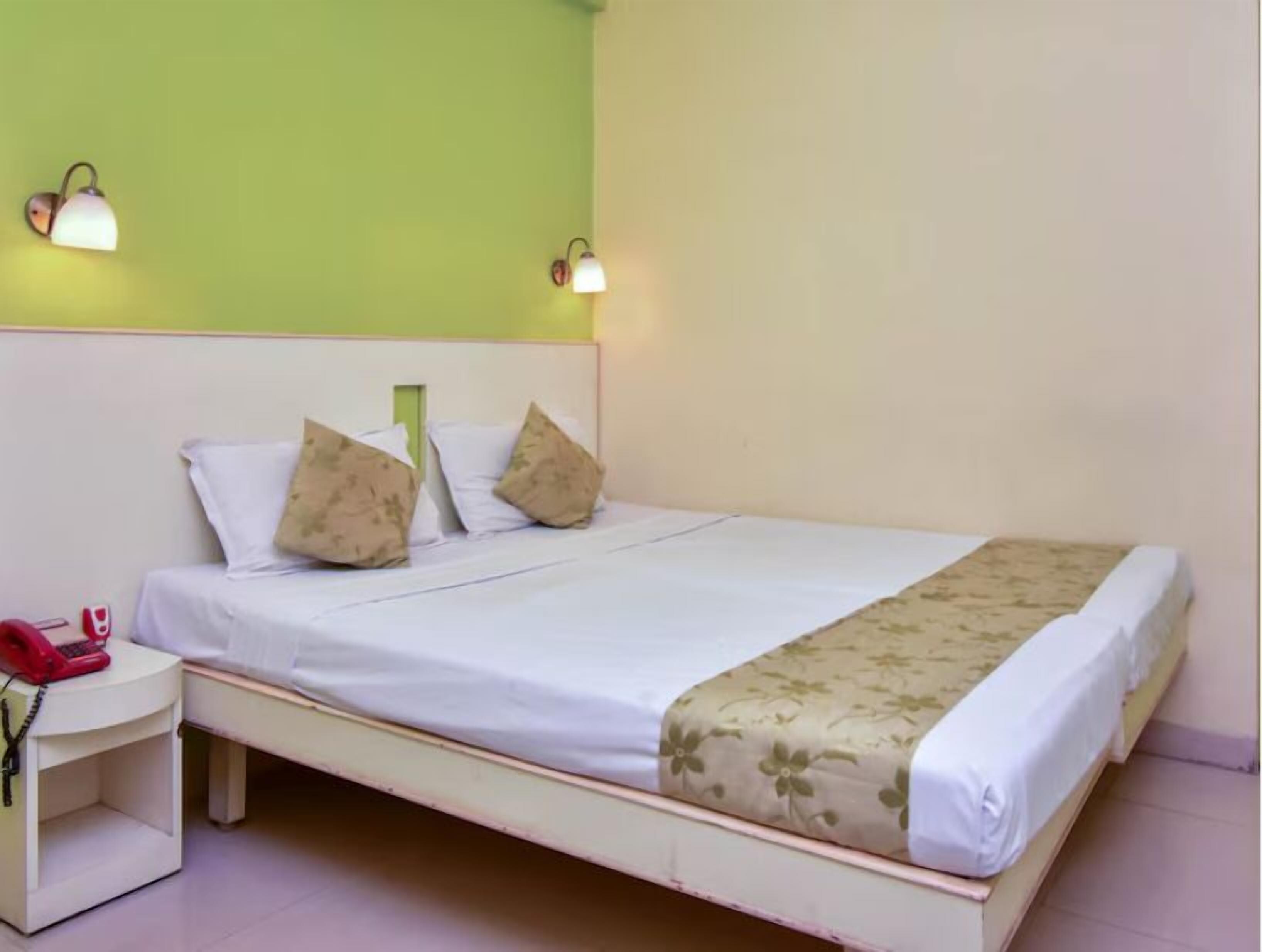 A single bed with white bedding, two wall-mounted lamps, and a small bedside table with a red telephone.