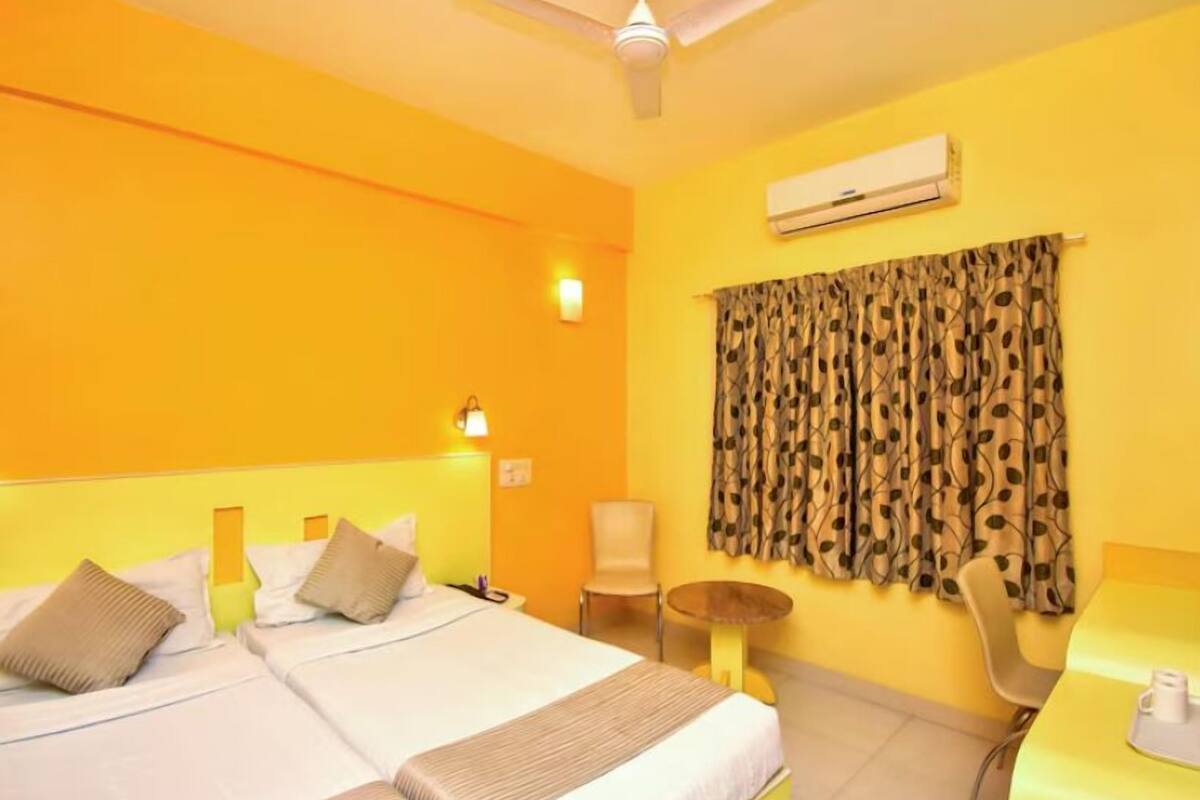 A hotel room with two beds, a desk, a chair, an air conditioning unit, and a ceiling fan.