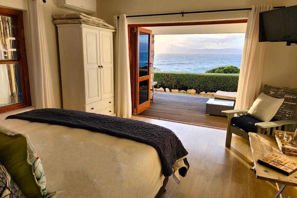 Een slaapkamer met een groot bed, een kledingkast en uitzicht op de zee door een open deur.
