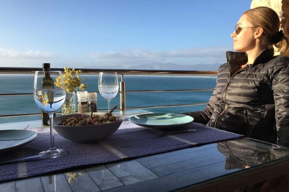 Een eettafel met een glas water, een wijnfles en een saladekom, met uitzicht op een prachtig zeegezicht.