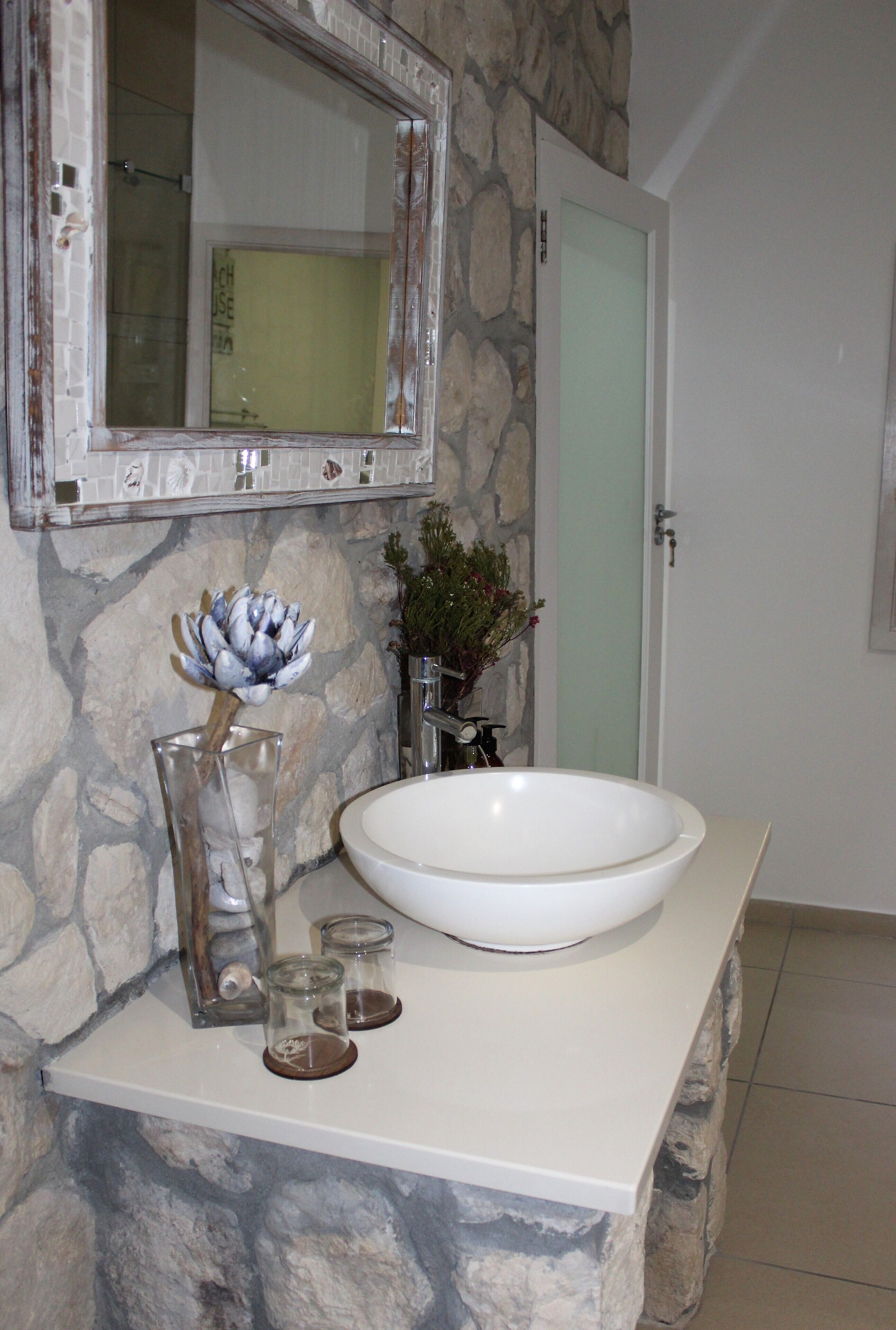 Un baño con pared de piedra, un lavamanos blanco y un espejo.