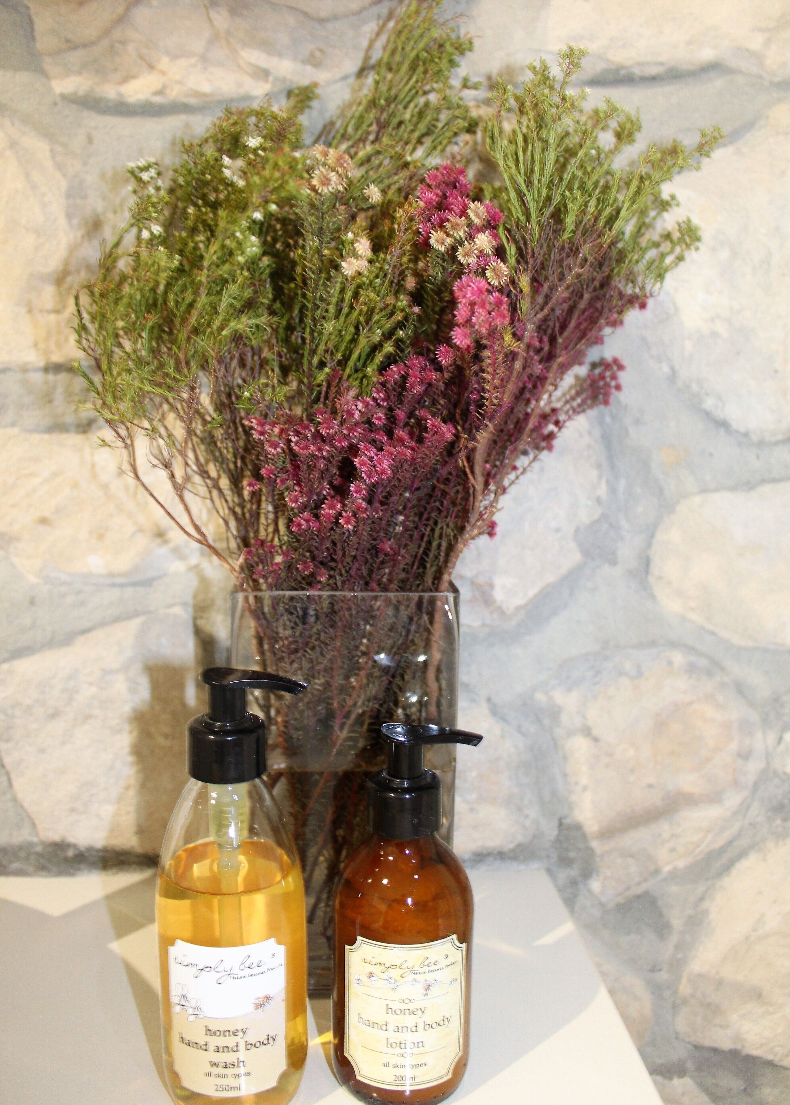 Two bottles of honey hand and body lotion and a glass vase with dried flowers.