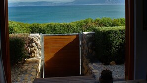 Une vue d’un paysage côtier, aperçue à travers une porte en bois, avec un jeu de société en bois posé sur une table au premier plan.