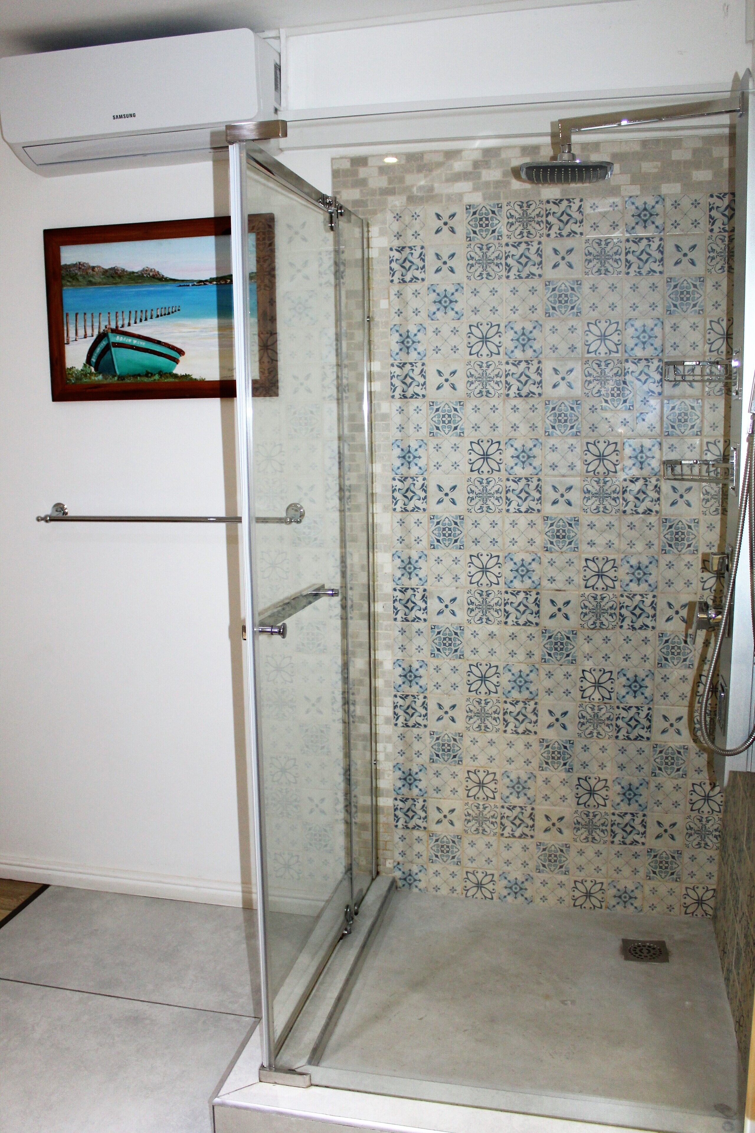 A glass-enclosed shower with a tiled wall featuring a blue and white pattern.