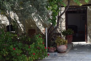 Un bâtiment en pierre avec une porte d’entrée, des plantes en pot et un poteau métallique.